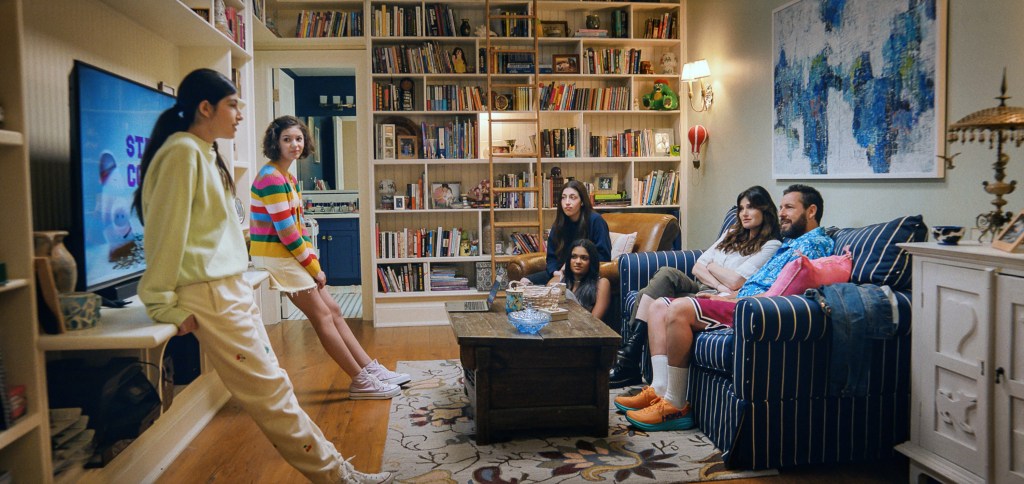 Sunny Sandler, Samantha Lorraine, Sadie Sandler, Zaara Kuttemperoor, Idina Menzel, and Adam Sandler gathered in a living room. 