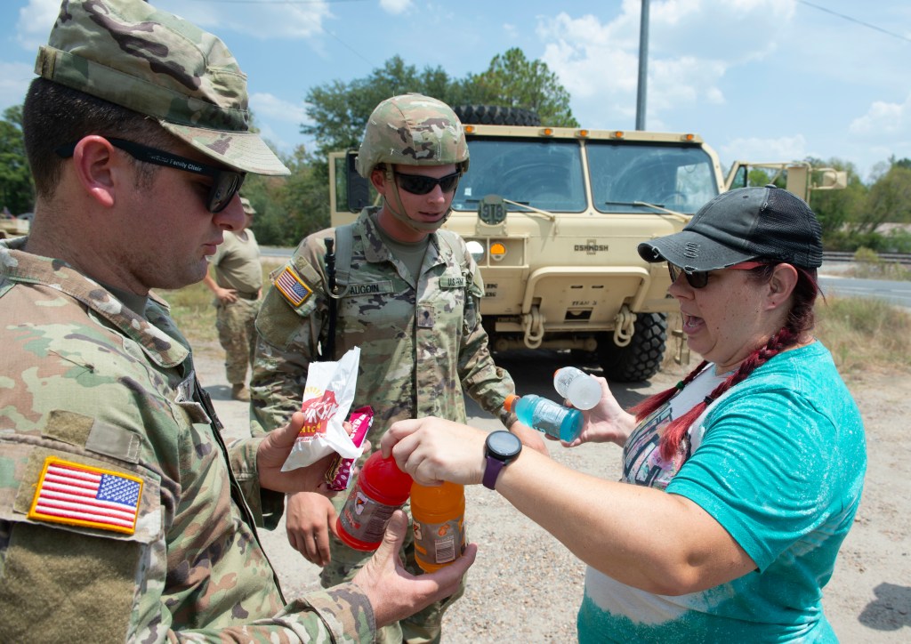 Volunteer Christina Brumley, right, drops off snacks and cold drinks to Army National Guard members Brian Aucoin, center, and Jacob Cox.