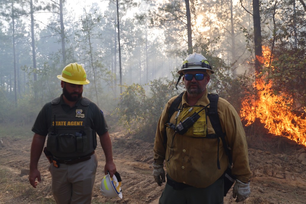Firefighters are pictured on the frontlines with a fire behind them.
