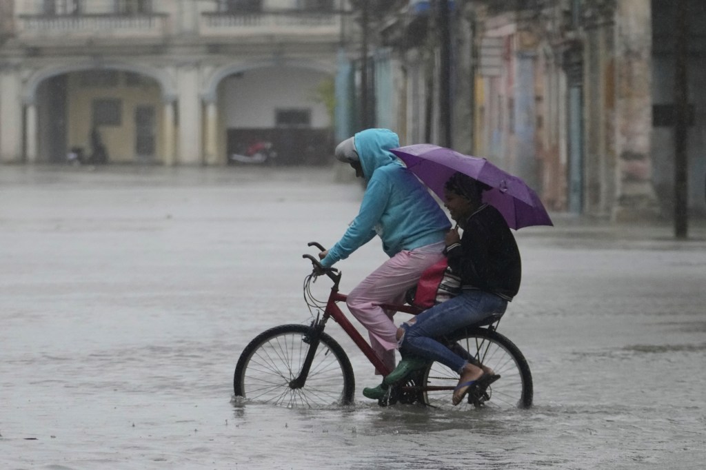 Commuters cycle through a street flooded by rain brought by Hurricane Idalia.