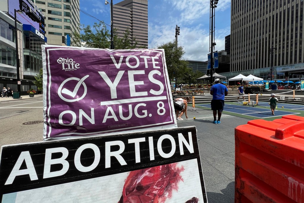 A sign asking Ohioans to vote in support of Issue 1 sits above another sign advocating against abortion rights at an event hosted by Created Equal on July 20, 2023, in Cincinnati, Ohio