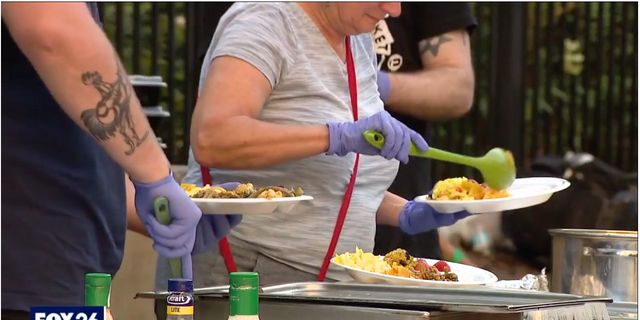 A volunteer can be seen scoops food into a plate outside the Houston Public Library downtown