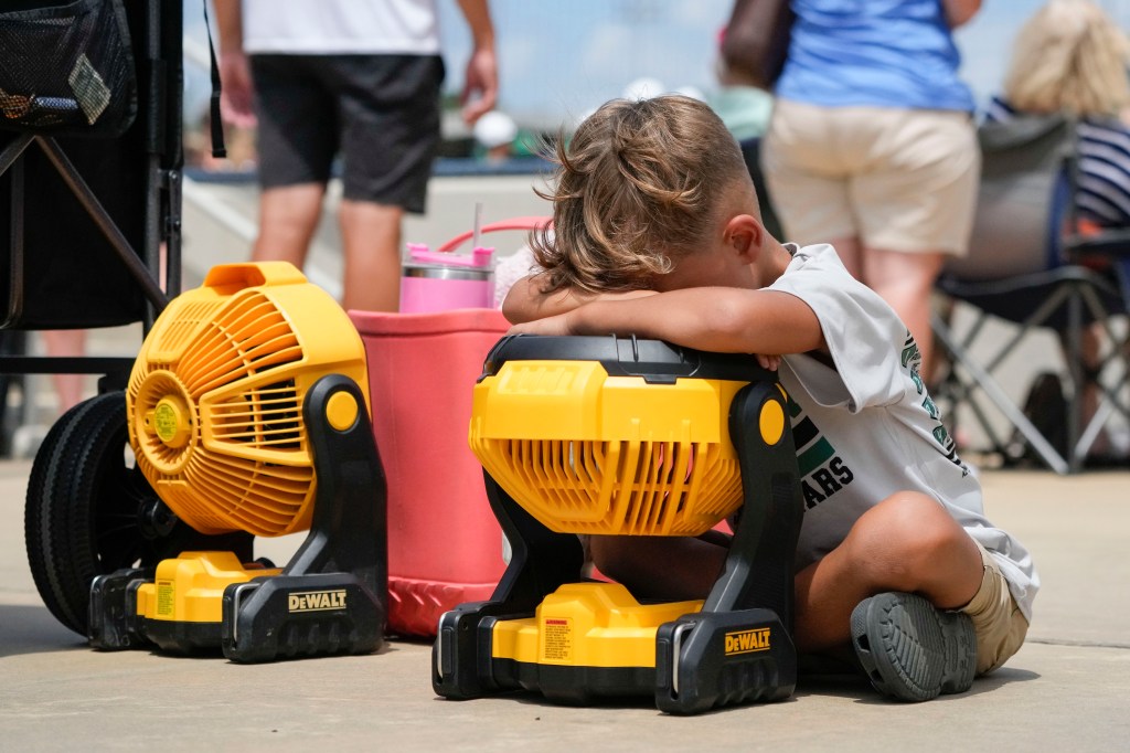 A kid lays his head on a portable fan to cool off during a youth baseball game in Ruston, Louisiana on Aug. 9, 2023.