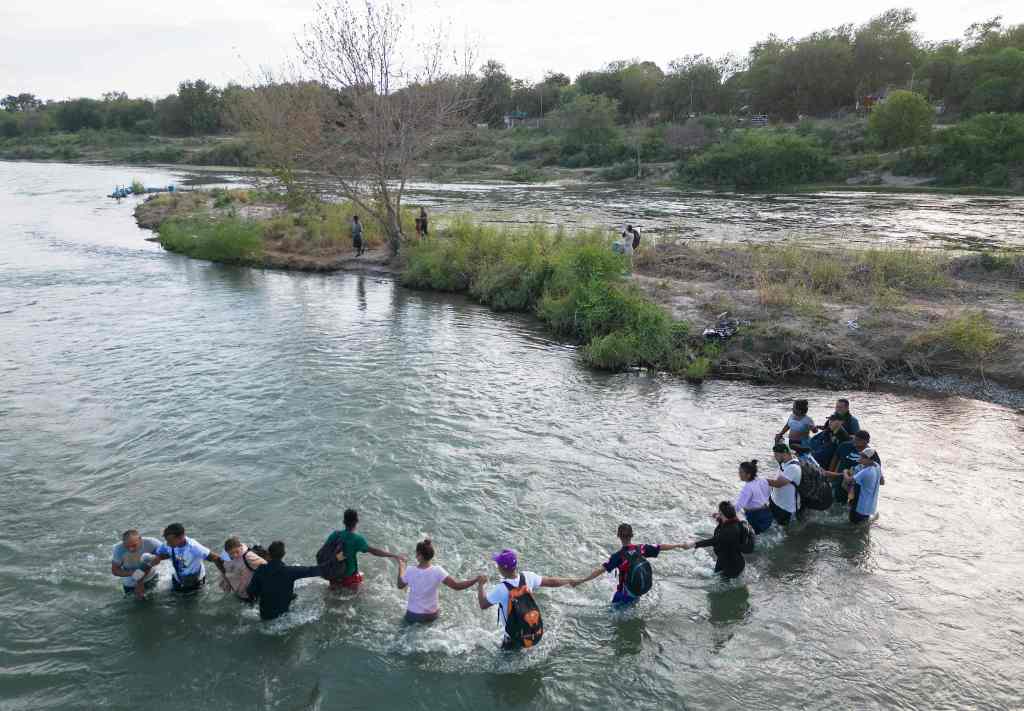 This aerial picture taken on September 24, 2023 shows a group of migrants holding hands as they cross the Rio Grande river at the US-Mexico border to Eagle Pass, Texas.