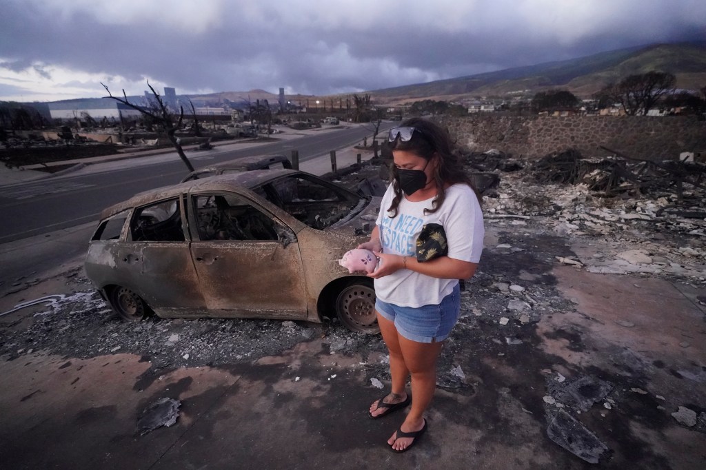 Summer Gerling picks up her piggy bank found in the rubble of her home following the wildfire on Aug. 10, 2023, in Lahaina, Hawaii.