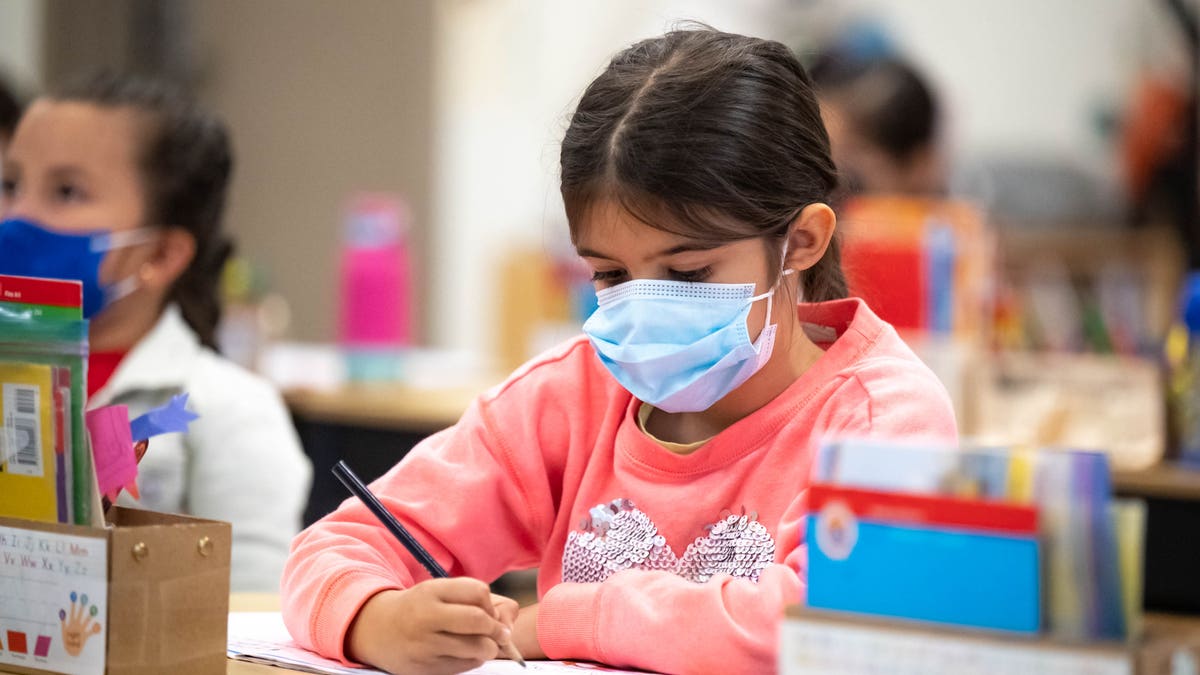 student wearing masks writes on paper