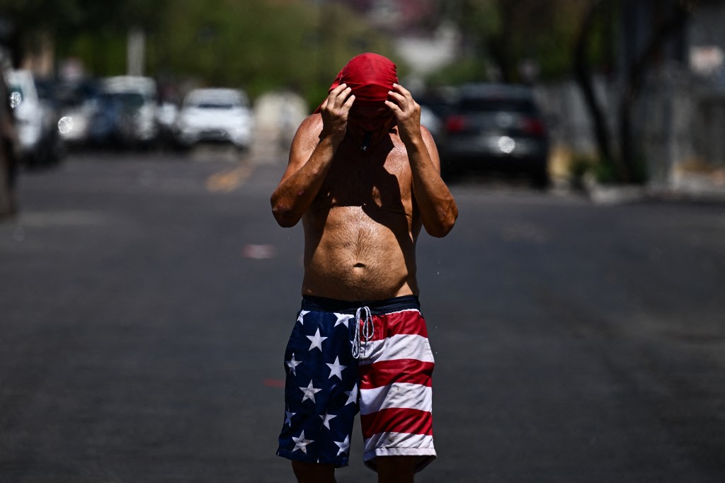 Water drips from a person as they grasp at their head covering while walking in the sun through "The Zone," a vast homeless encampment where hundreds of people reside, during a record heat wave in Phoenix, Arizona on July 18, 2023.