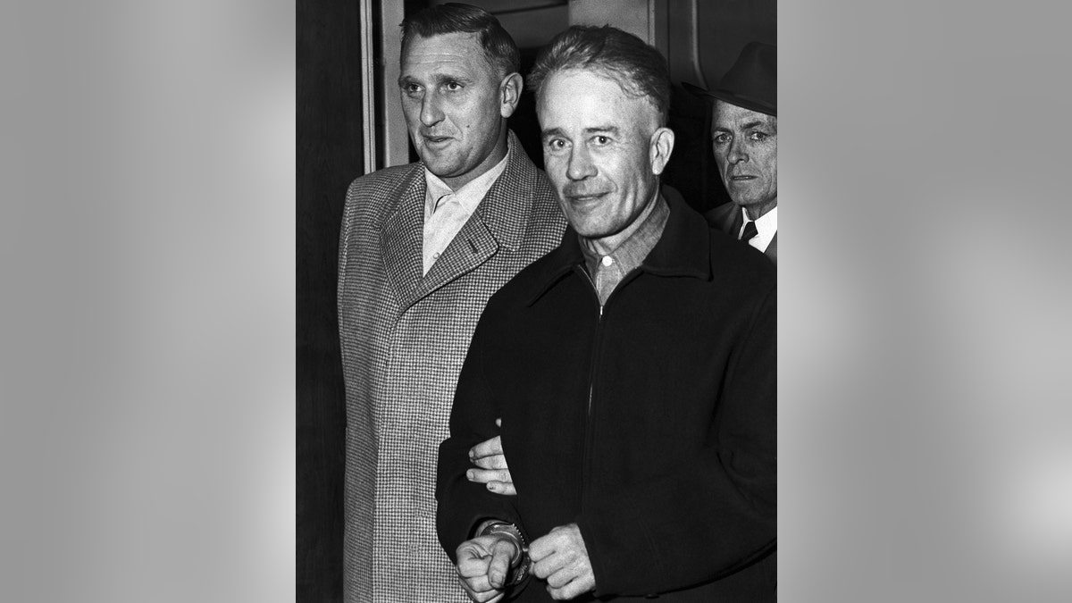 Ed Gein wearing a dark coat being escorted by police