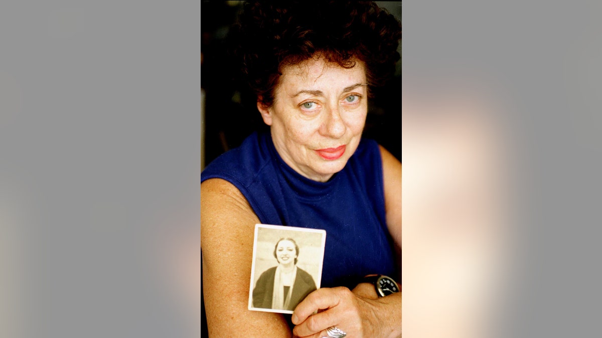 A woman wearing a blue sleeveless sweater holding a black and white photo