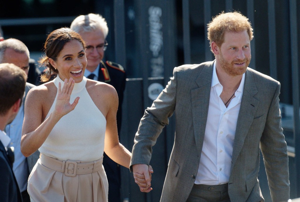 Photo of Meghan Markle and Prince Harry holding hands together, while Meghan waves. 