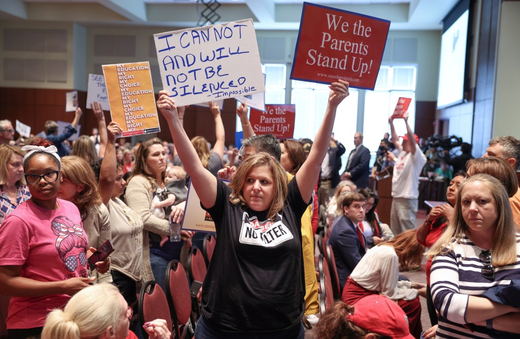 A woman holds up signs that say "I can not and will not be silenced" and "We the Parents Stand Up" during a protest at a school board meeting in Virginia.