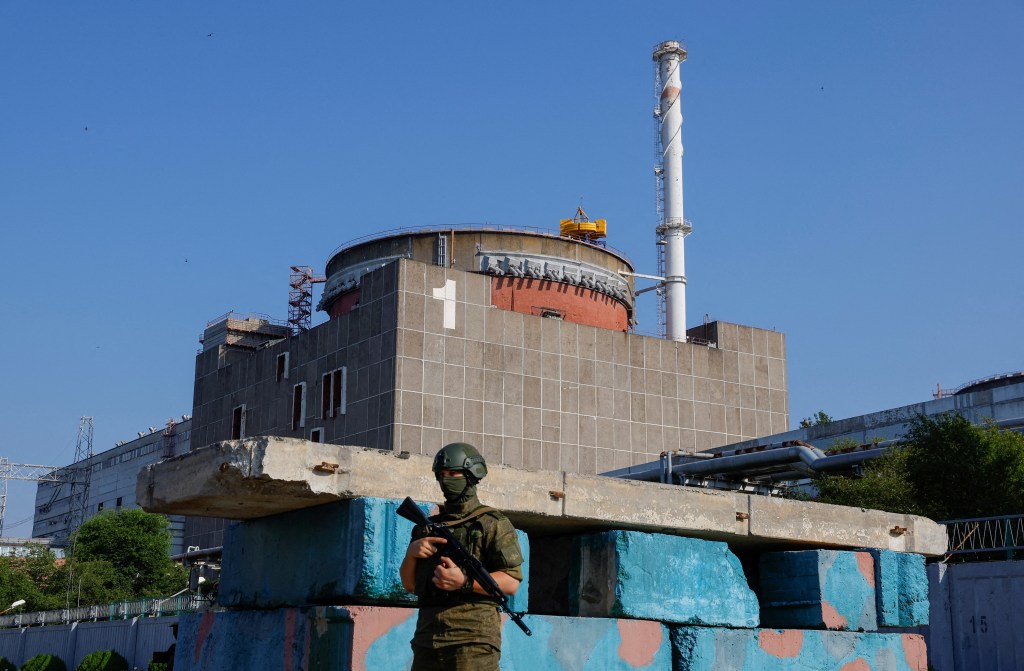A man wearing a helmet and green military clothing and carrying a gun walks outside the Zaporizhzhia power plant.