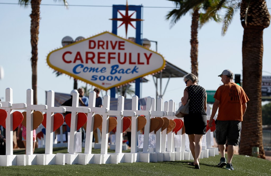 People walk by crosses placed near Las Vegas' famous sign Thursday, Oct. 5, 2017, in Las Vegas.