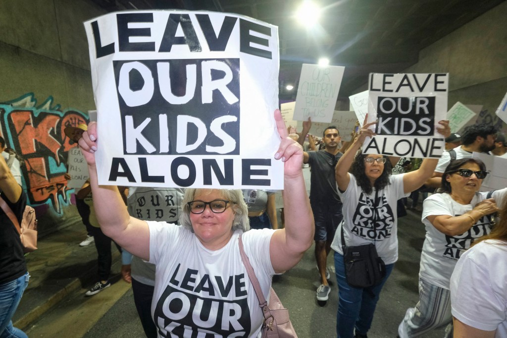 Several parents hold up signs that say, "Leave our kids alone," the same slogan seen on their t-shirts, during a protest in Lon Angeles in August.