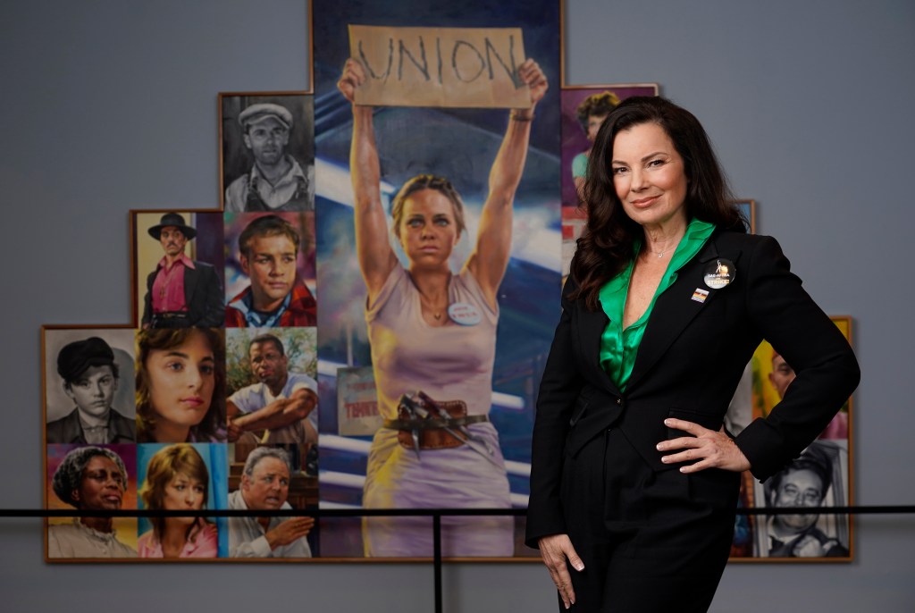 SAG-AFTRA President Fran Drescher stands in front of a montage of movie and television images dominated by Sally Field holding a sign that says, "Union," from the film, "Norma Rae."