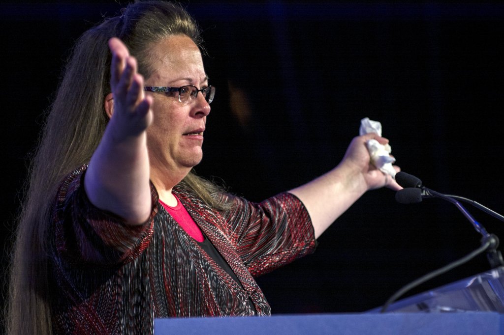 Kim Davis outstretches her arms at a podium with a microphone. 