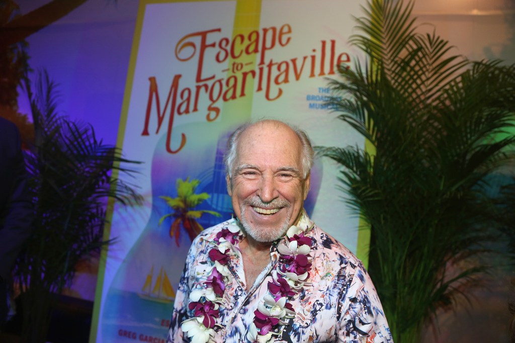 Singer Jimmy Buffett stands smiling in front of a poster for his Broadway musical "Escape to Margaritaville," at the show's opening night.