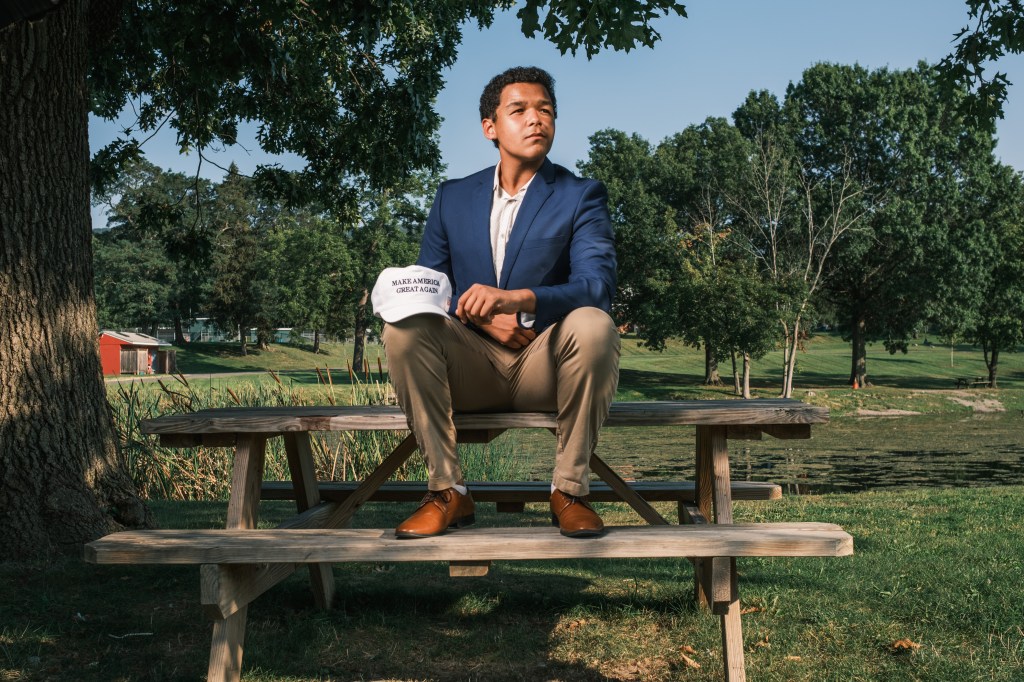 Elias Cunningham sitting on a picnic table, holding a "Make America Great Again" hat. 