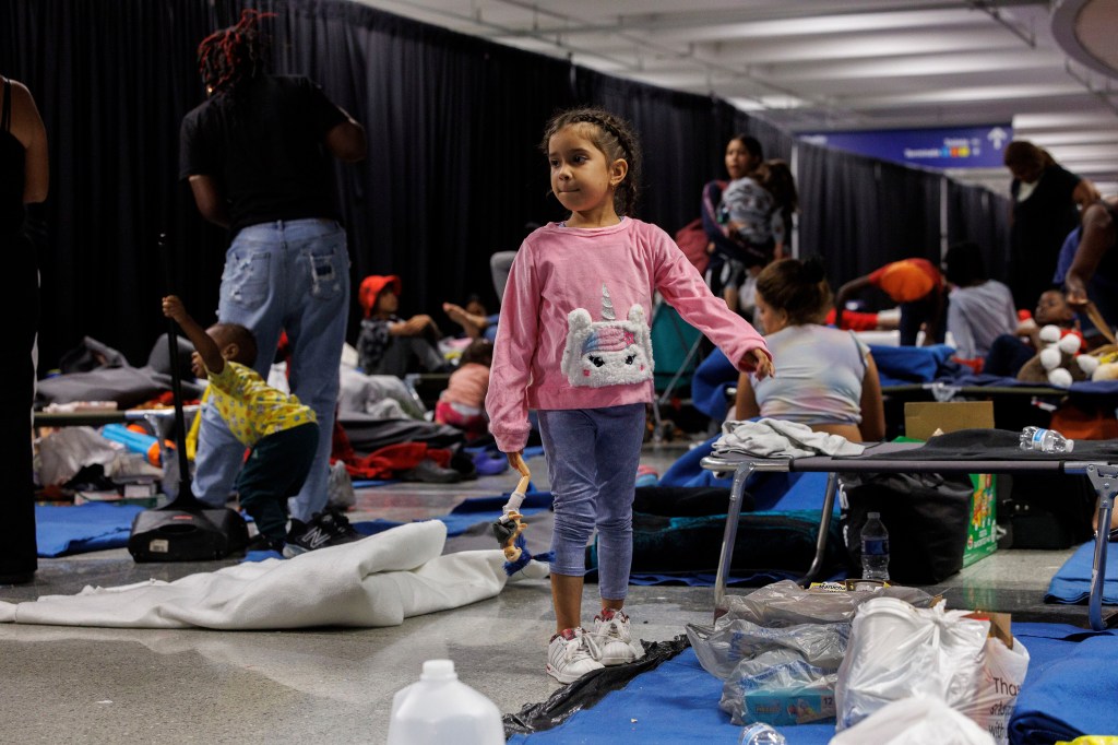 A young child plays with a doll while other recently arrived migrants sit on cots and the floor inside O'Hare International Airport on Aug. 31.