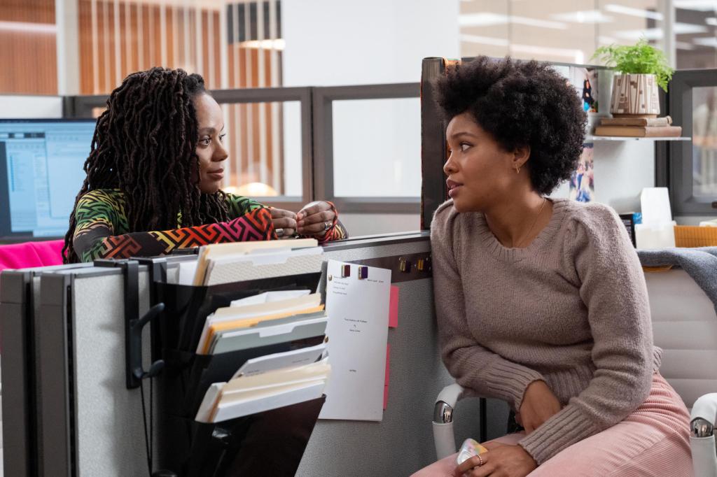 Hazel (Ashleigh Murray) and Nella (Sinclair Daniel) smiling at each other over a cubicle in "The Other Black Girl." 