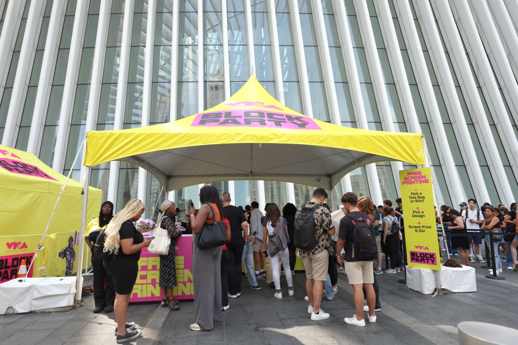 Fans gathered under a tent on a sidwalk. 