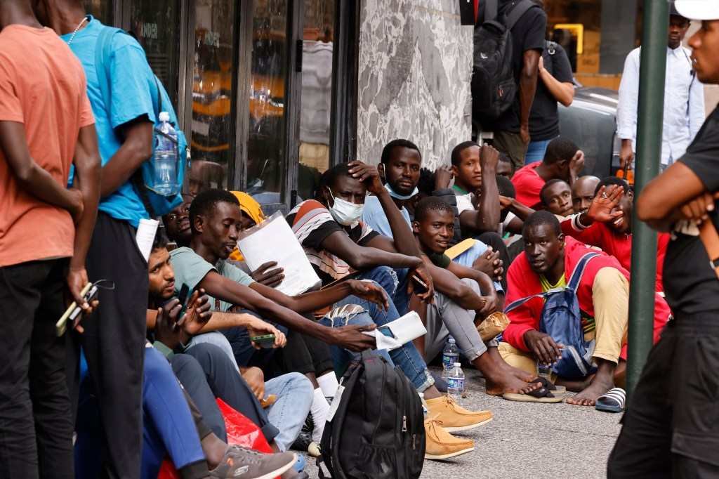 Migrant men are seen here sitting on the sidewalk in New York City waiting to be processed.