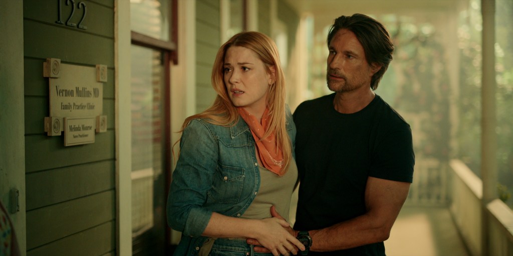 Alexandra Breckenridge and Martin Henderson as Mel and Jack. They're standing on the porch of Doc Mullins' office and look concerned. They're clasping hands on Mel's waist.