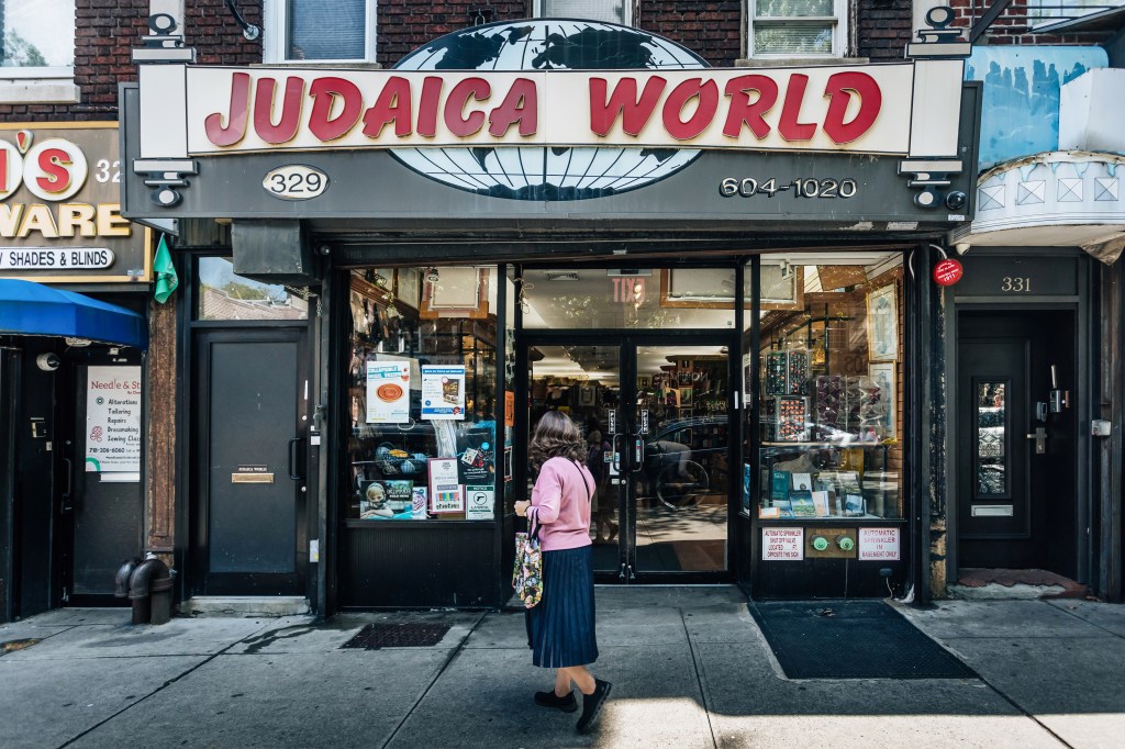 Storefront of Judaica World in Crown Heights, Brooklyn, with a woman standing outside