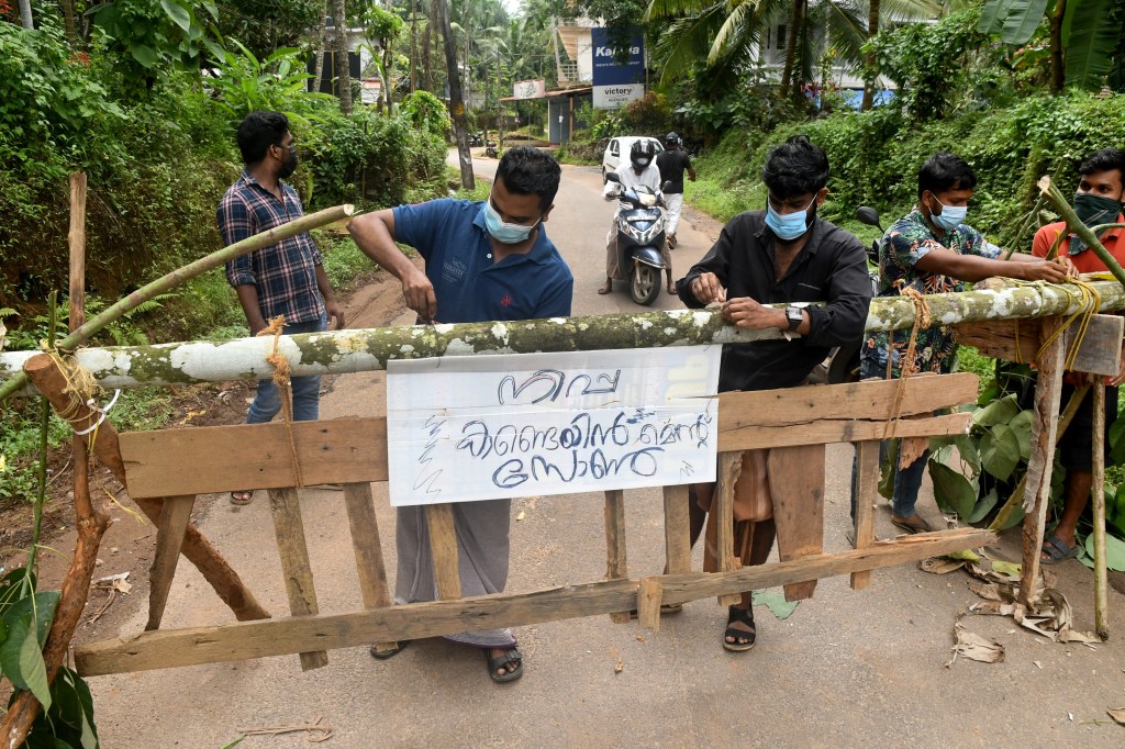 Residents fix a sign reading "Nipah containment zone" on a barricade put up to block a road after authorities declared the area a quarantine zone.