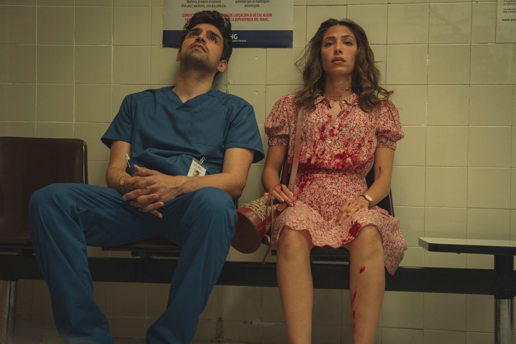 Jordi and Erin are sitting on a bench. Erin is wearing a dress that's covered in blood. Jordi is wearing his nurse's scrubs and is looking skyward with an exasperated look. His arms are crossed on his knees.