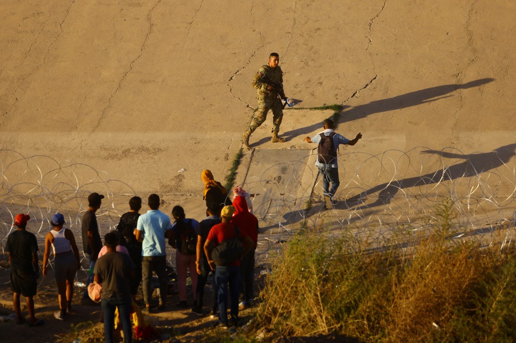 A member of the Texas National Guard tries to inhibit the crossing of a migrant into the United States.