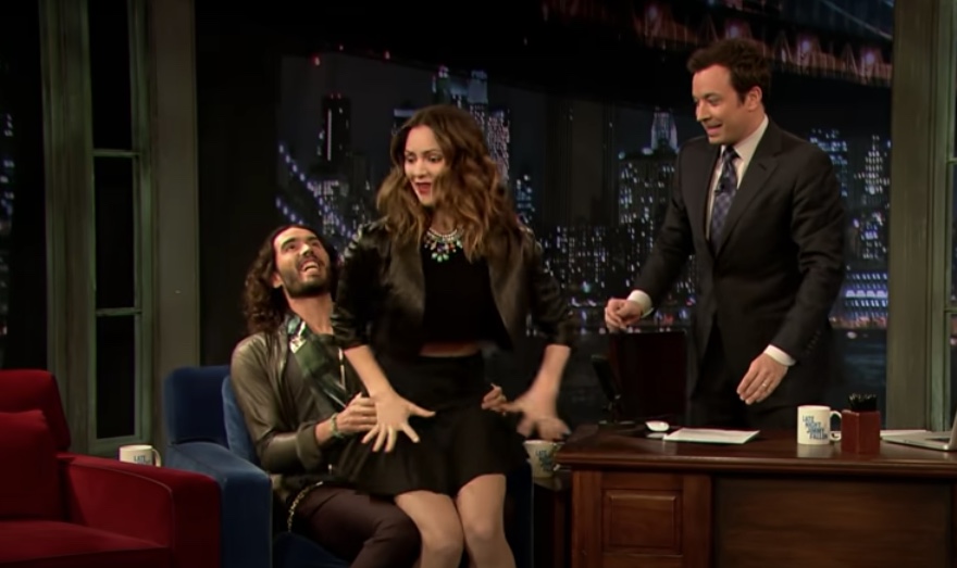 Russell Brand bounces Katharine McPhee on his lap during "The Tonight Show" in 2013. She looks very uncomfortable and is trying to get away, while Jimmy Fallon looks on, disturbed.