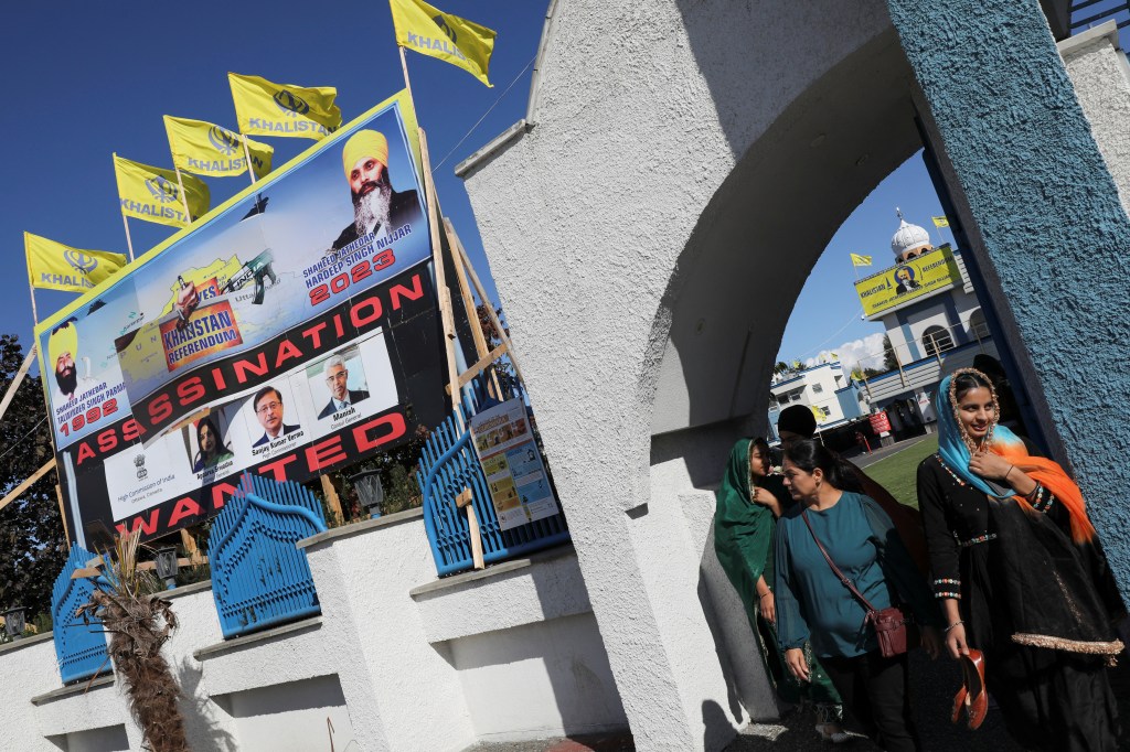 People walk as a sign outside the Guru Nanak Sikh Gurdwara temple is seen after the killing on its grounds in June 2023 of Sikh leader Hardeep Singh Nijjar