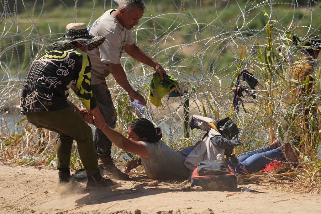 A migrant who crossed into the U.S. from Mexico is pulled under concertina wire along the Rio Grande river, Thursday, Sept. 21, 2023, in Eagle Pass, Texas. 