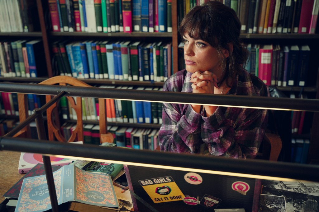 Mave (Emma Mackey) in a library looking serious. 
