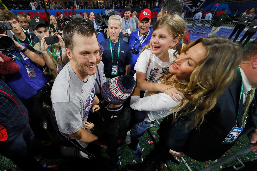 Gisele and Tom Brady holding their daughter at a game. 