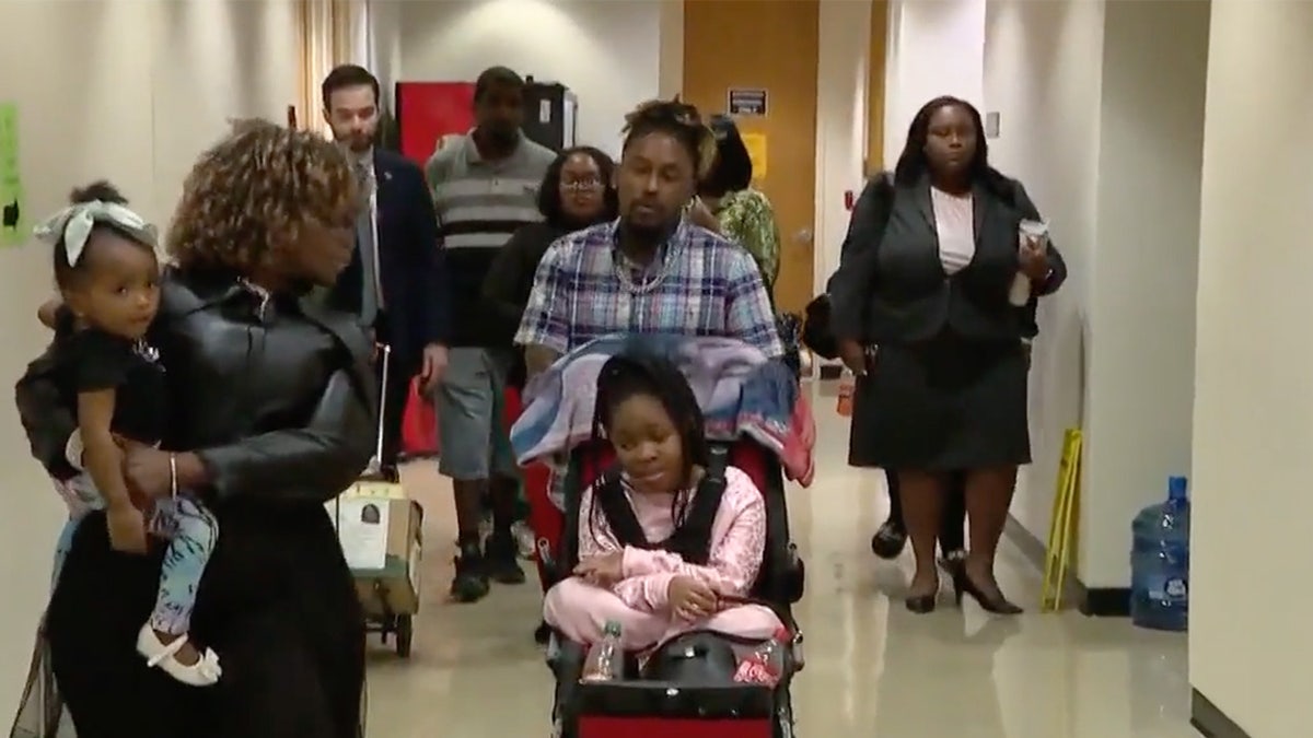 A group of people walk down a courtroom corridor.