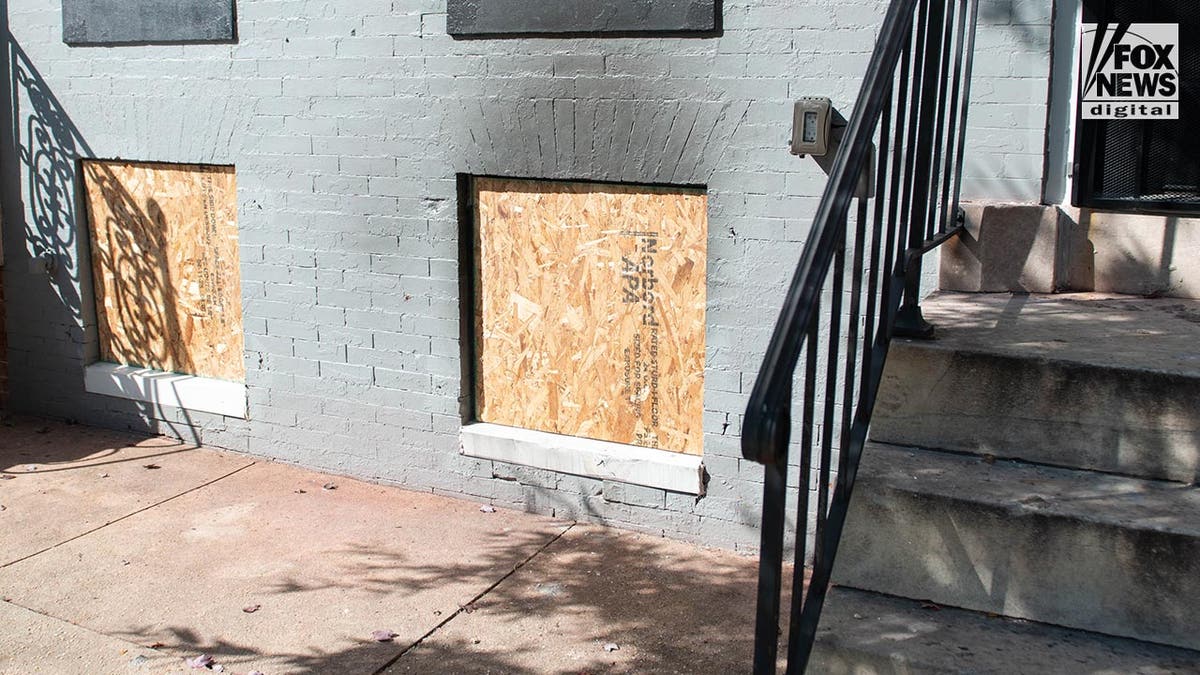 Exterior view of a townhouse painted grey with boarded up windows