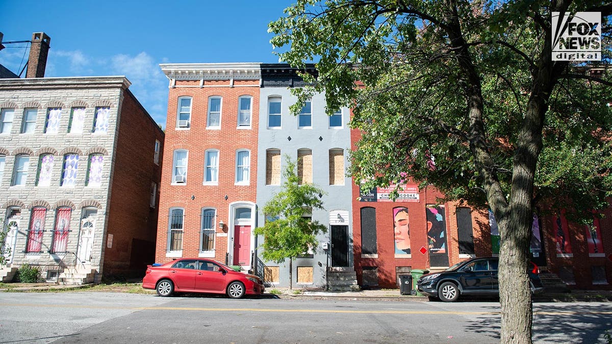 Exterior view of a townhouse painted grey with boarded up windows