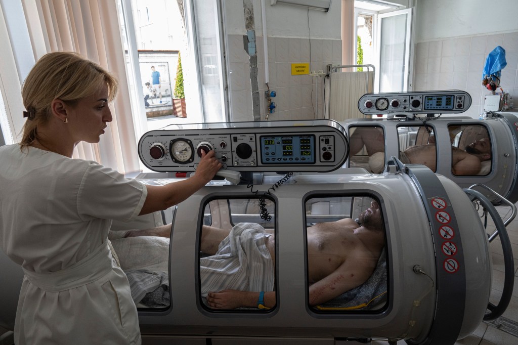 An anesthesiologist sets up a hyperbaric chamber for a Ukrainian serviceman during his treatment at St. Panteleimon hospital in Lviv, Ukraine. 