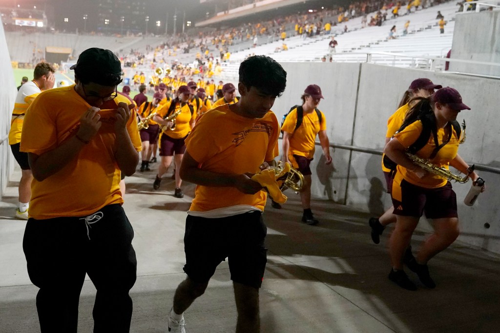 Members of the Arizona State student section and the band take cover during the weather delay in the team's NCAA college football game against Southern Utah on  Aug. 31, 2023, in Tempe, Ariz.