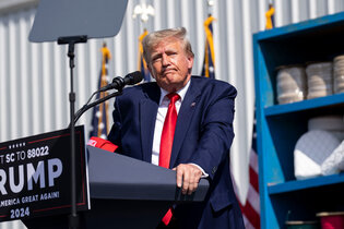 Donald Trump standing behind a dais on an outdoor stage.