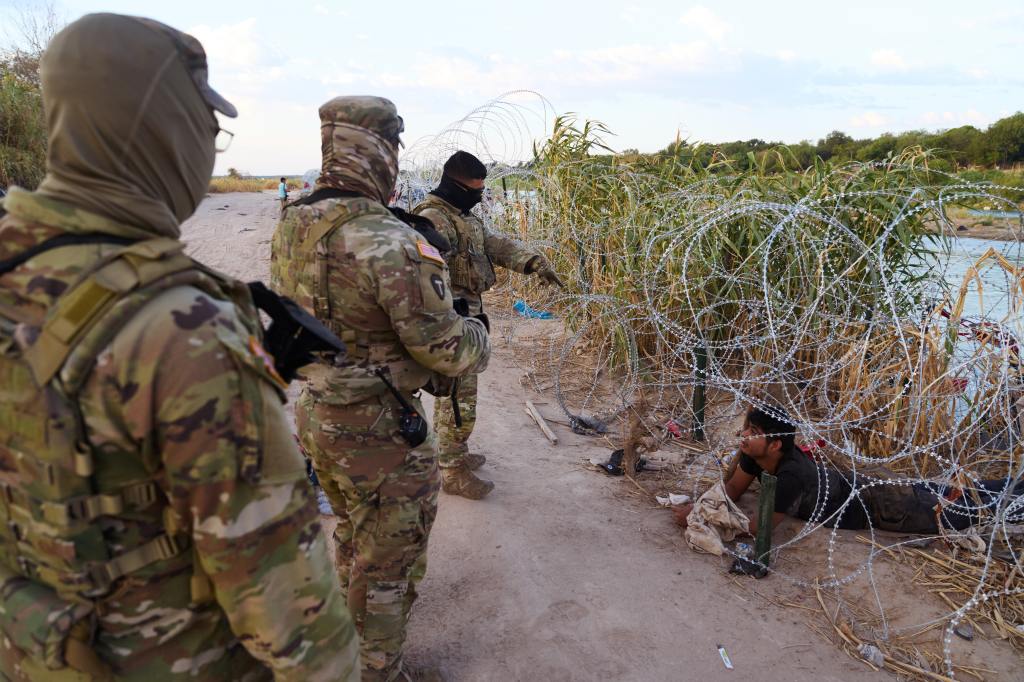 A migrant tries to pass under concertina wire after he crossed the Rio Grande river from Mexico into the United States on Monday, September 25, 2023