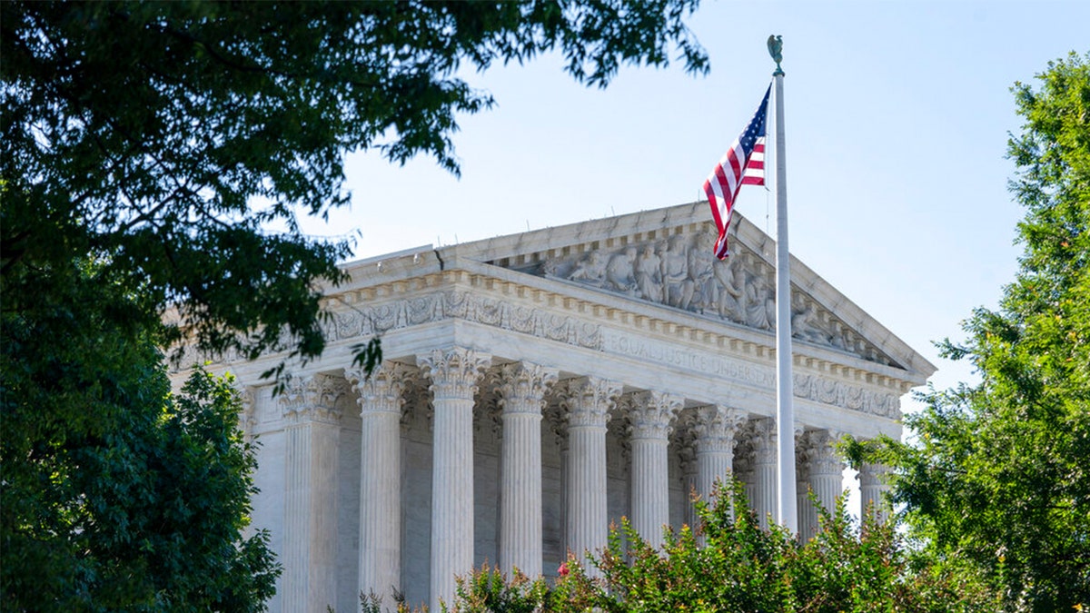 US Supreme Court building framed by trees, US flag out front