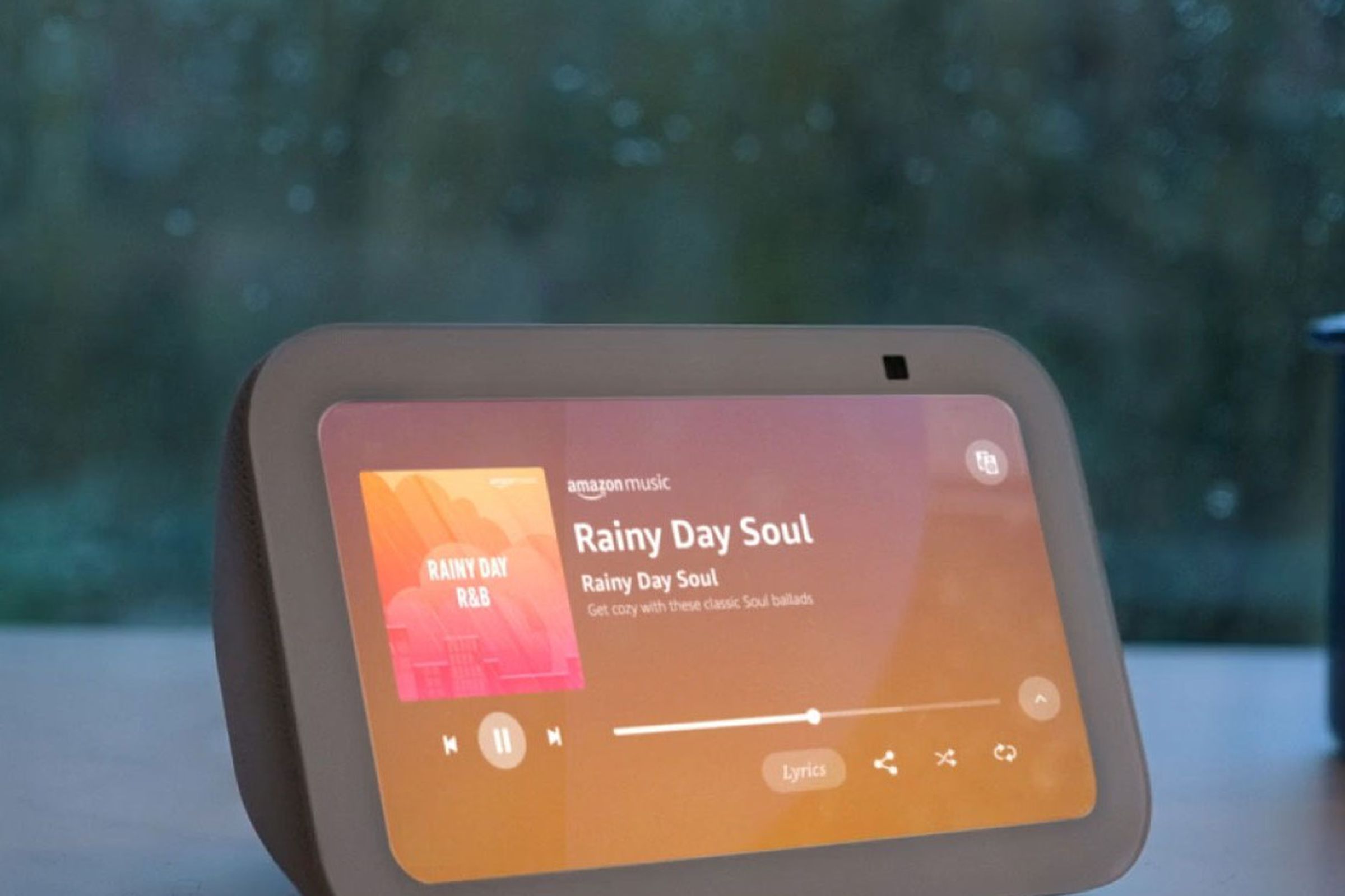 The third-gen Echo Show 5 turned on while on a desk in front of the window during a rainy day.