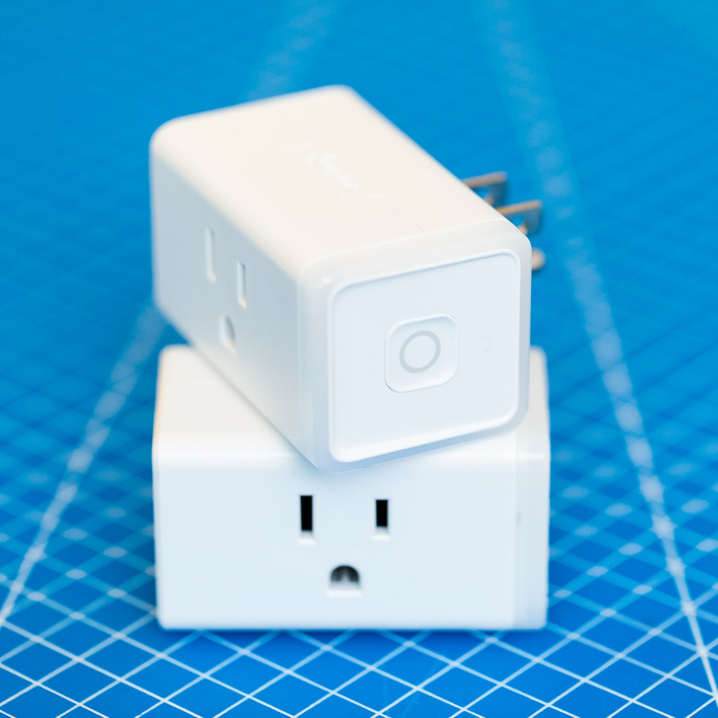 Two TP-Link Kasa KP125M Matter smart plugs stacked on top of each other. They are white rectangular prisms with a three-prong outlet on the front face and three-prong plug on the rear face, TP-Link on the top face, and a power button on the right face.