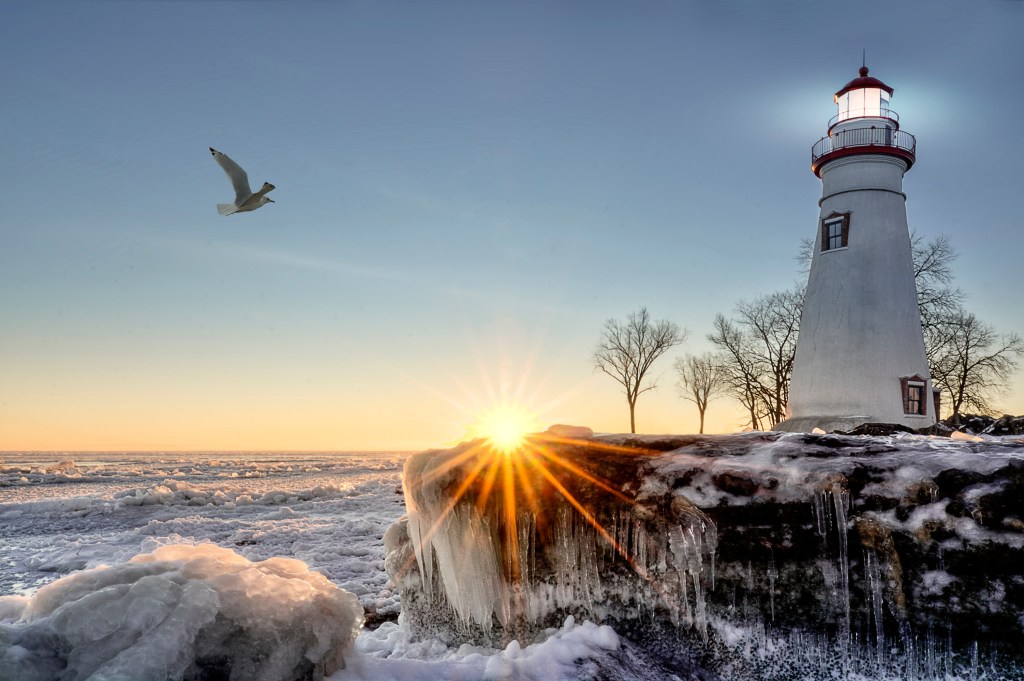 The historic Marblehead Lighthouse in Northwest Ohio sits along the rocky shores of the frozen Lake Erie. Seen here in winter with a colorful sunrise and snow and ice.