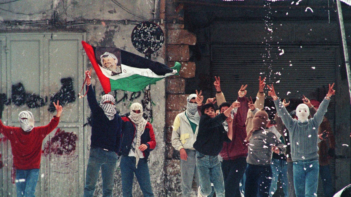 Masked Hamas terrorists stand in front of a mural of assassinated Hamas leaders Sheikh Ahmed Yassin and Abdel Aziz al-Rantissi.