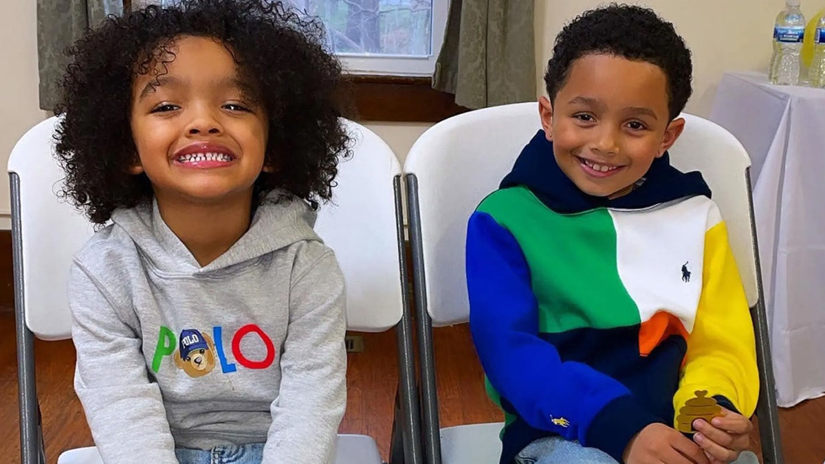 Two little boys sit in chairs smiling.