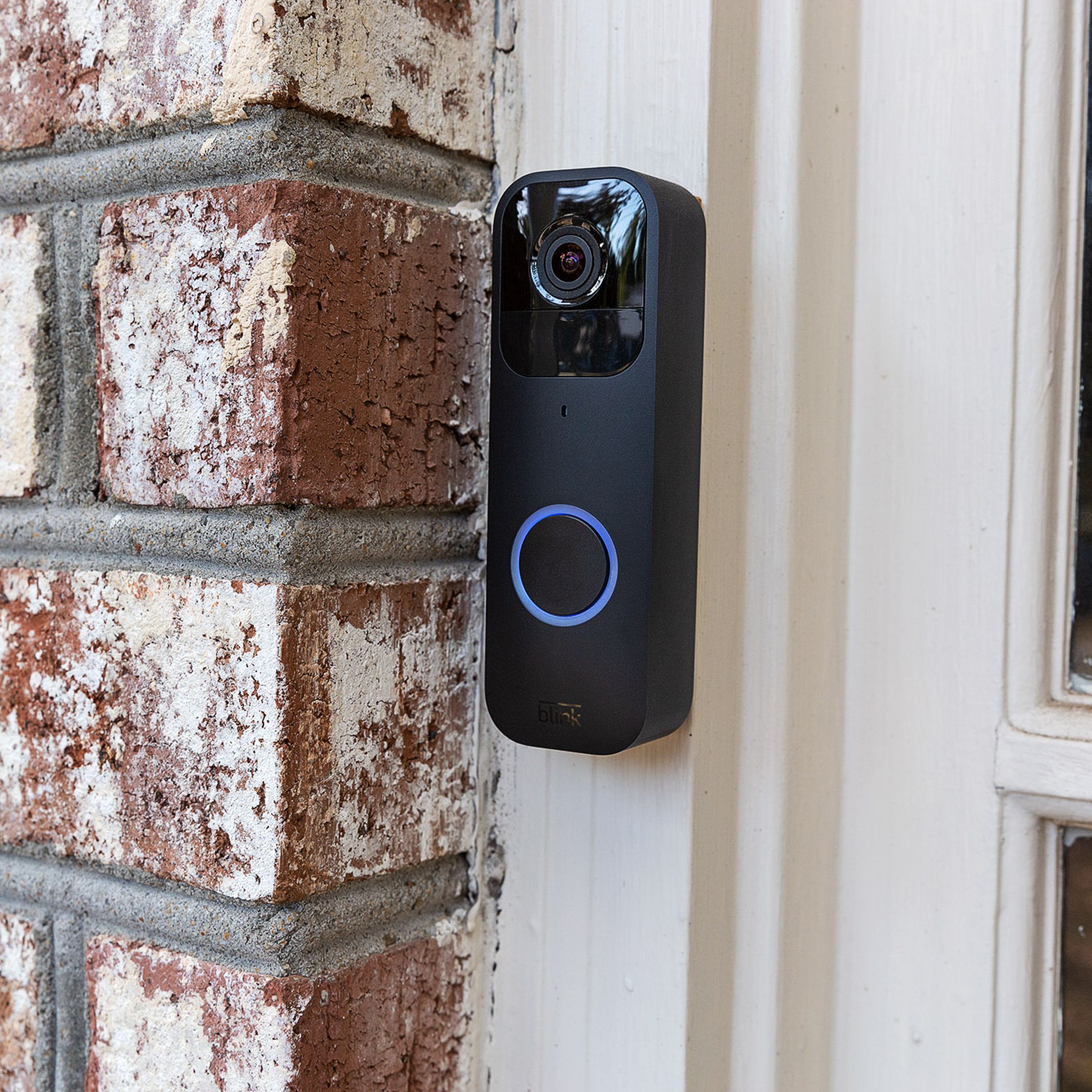 The black Blink Video Doorbell hung up on a brick wall outside of a house.